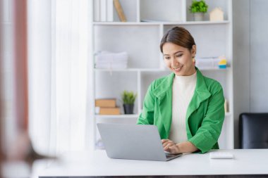 Masa başında dizüstü bilgisayar kullanarak çalışan Asyalı kadın çalışanlar harcamaları hesaplıyor, ofisteki grafik veri tablosundaki mali raporlar