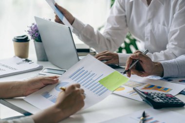 İş adamları mali raporları analiz ediyor ve hesap makinesi kullanıyorlar. Muhasebe hesaplamaları ve ortaklar şirketin satış planlarını analiz etmek için mali raporlara işaret ediyor..