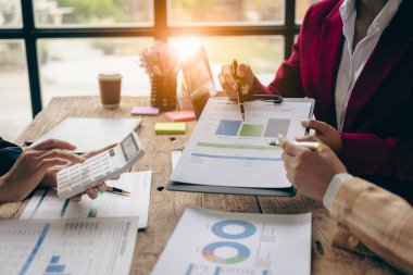 İş adamları mali raporları analiz ediyor ve hesap makinesi kullanıyorlar. Muhasebe hesaplamaları ve ortaklar şirketin satış planlarını analiz etmek için mali raporlara işaret ediyor..