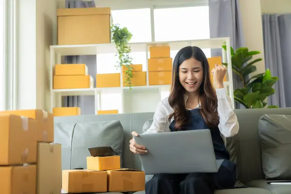 Happy Asian woman receives good news from online name order, SME parcel box and uses smartphone to order online email in SME seller chat box, concept