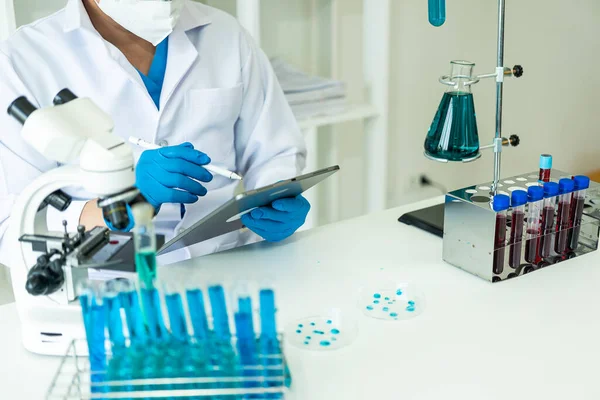 化学実験室でDna分子を検査するマスクの医師 化学実験室の研究者で顕微鏡で液体サンプルを調べる科学者 — ストック写真