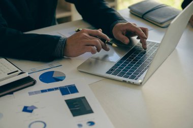 Genç Asyalı iş adamı dizüstü bilgisayarla çalışıyor, grafikleri, şirket bütçe raporlarını, üretim kontrolünü kontrol ediyor. İşletim denetim maliyeti artı fiyat yakın plan resimleri