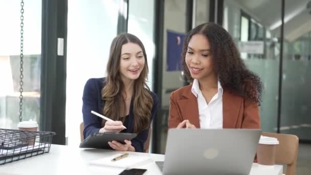 アフリカの女性オフィスワーカーとブロンドの同僚は財務報告について話し合っている 会社の会計分析について話している2人の若い女性の屋内ショット — ストック動画
