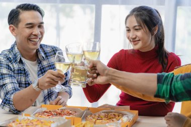 Arkadaşlarıyla birlikte mutlu Asyalı gençler parti, yemek, pizza, çatal bıçak takımlı atıştırmalıklar ve lezzetli yiyecekler eşliğinde kadeh tokuşturmayı kutluyor.