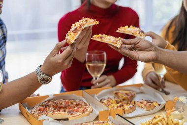 Arkadaşlarıyla birlikte mutlu Asyalı gençler parti, yemek, pizza, çatal bıçak takımlı atıştırmalıklar ve lezzetli yiyecekler eşliğinde kadeh tokuşturmayı kutluyor.