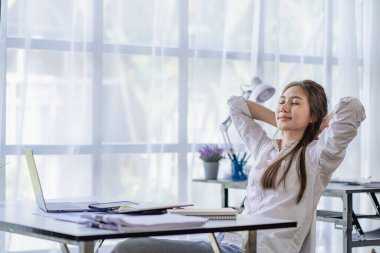 Önünde dizüstü bilgisayarla oturan mutlu, rahat, rahat bir kadın. Kolları başının üstünde, yaşam tarzı, refah ve sağlık kavramı..