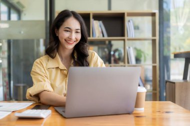 Evden çalışan hırslı Asyalı kız dizüstü bilgisayar ekranlarına ve mali belgelere bakıyor, kadın uzaktan çalışırken e-postaları kontrol ediyor veya araştırma yapıyor.