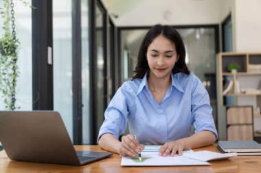 Evden çalışan hırslı Asyalı kız dizüstü bilgisayar ekranlarına ve mali belgelere bakıyor, kadın uzaktan çalışırken e-postaları kontrol ediyor veya araştırma yapıyor.