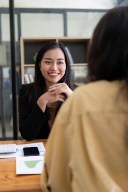 Dizüstü bilgisayarlar ve finansal belgelerle çalışan iki Asyalı kadın pazarlama planlarını tartışıyor. Yeni şirketin satış stratejisi güncel olaylarla uyumlu.