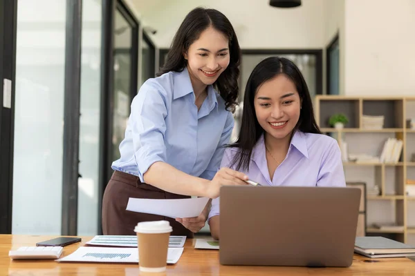两名持有笔记本电脑和财务文件的亚洲妇女正在讨论营销计划 这家新公司的销售策略符合当前形势 — 图库照片