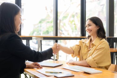 Anlaşmayı başaran iki Asyalı iş kadını el sıkışıyor. Toplantıda iş ortaklarının el sıkışması kavramı