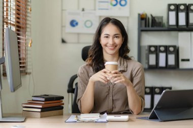 Serbest ofiste tabletle çalışan Asyalı bir kadın. Genç Asyalı bir kadın. Bir kahvecinin ahşap masasında dizüstü bilgisayarlı ve tabletli bir yazı yazıyor..