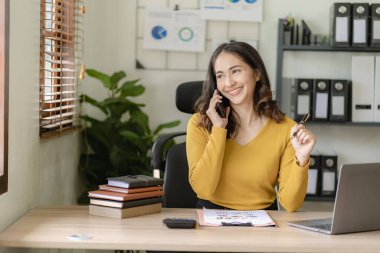 Serbest ofiste tabletle çalışan Asyalı bir kadın. Genç Asyalı bir kadın. Bir kahvecinin ahşap masasında dizüstü bilgisayarlı ve tabletli bir yazı yazıyor..