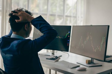 Adam bilgisayar başında elleri ile inliyor ve ekranda başarısız iş grafiği ile kripto para birimi fiyatlarını takip eden kripto para birimi grafiği ile ekranda inliyor.
