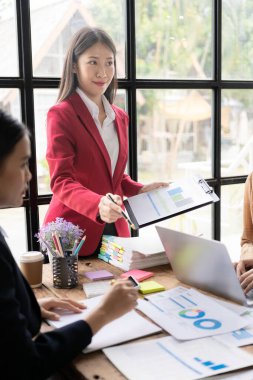 Müşterilerle konuşan ve ofis masasındaki müşterilere yatırım raporlarını gösteren, veri, bütçe çizelgeleri veya yasal sonuçları gösteren mutlu genç bayan finans danışmanı..