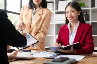 Müşterilerle konuşan ve ofis masasındaki müşterilere yatırım raporlarını gösteren, veri, bütçe çizelgeleri veya yasal sonuçları gösteren mutlu genç bayan finans danışmanı..