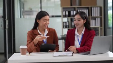 İki genç Asyalı iş kadını ofiste mali belgeler üzerinde çalışarak finansal istatistikleri dizüstü bilgisayarlarla analiz ediyorlar. Şirketin bütçesini ve muhasebesini planla.