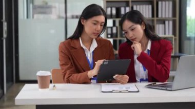 İki genç Asyalı iş kadını ofiste mali belgeler üzerinde çalışarak finansal istatistikleri dizüstü bilgisayarlarla analiz ediyorlar. Şirketin bütçesini ve muhasebesini planla.