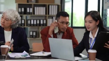 Asya iş dünyası finans ekibi proje beyin fırtınasında birlikte çalışıyor. İş birliği yapıyor ve stratejik planlama şirketi olarak çalışıyor. Finans belgeleri ve dizüstü bilgisayarı masada.
