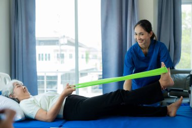 Huzurevindeki genç bir Asyalı hemşire yaşlı bir kadınla ilgileniyor. Uzman hekim, yaşlı hastaların sağlıkları için egzersiz yapmaları için fizik tedavi hizmetleri sunar..