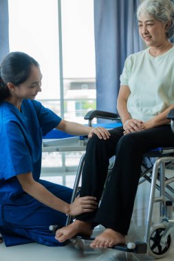 Huzurevindeki genç bir Asyalı hemşire yaşlı bir kadınla ilgileniyor. Uzman hekim, yaşlı hastaların sağlıkları için egzersiz yapmaları için fizik tedavi hizmetleri sunar..