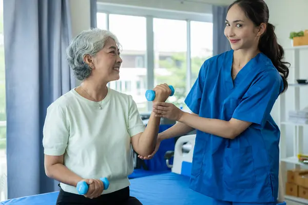 A young Asian nurse at a nursing home takes care of a senior woman. The attending physician provides physical therapy services for elderly patients to exercise for their health.