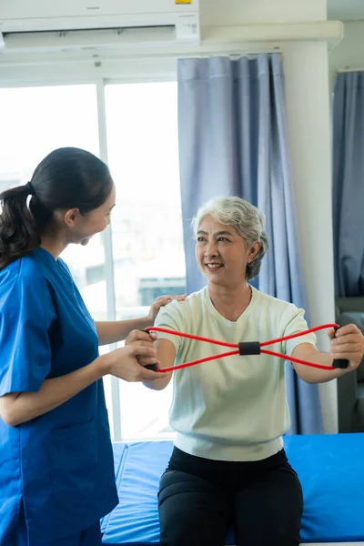 A young Asian nurse at a nursing home takes care of a senior woman. The attending physician provides physical therapy services for elderly patients to exercise for their health.