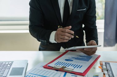 İş adamı, grafik ve grafik veri analizi için iş belgesine işaret ediyor ve elinde kalem tutan ve kar kavramını analiz etmek için mali belgeleri işaret eden muhasebe işkadını