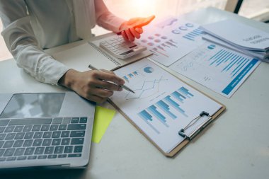 İş adamı, grafik ve grafik veri analizi için iş belgesine işaret ediyor ve elinde kalem tutan ve kar kavramını analiz etmek için mali belgeleri işaret eden muhasebe işkadını