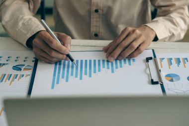 İş adamı, grafik ve grafik veri analizi için iş belgesine işaret ediyor ve elinde kalem tutan ve kar kavramını analiz etmek için mali belgeleri işaret eden muhasebe işkadını