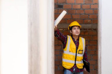 Genç Asyalı inşaat mühendisi ya da miğfer takan inşaat yöneticisi inşaat alanını incelerken yüzünü çeviriyor ve gülümsüyor..