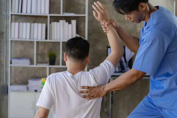 亚洲男性患者在护理人员的帮助下进行物理治疗有吸引力的护理人员帮助和支持手臂和肩部肌肉受伤的男性 — 图库照片