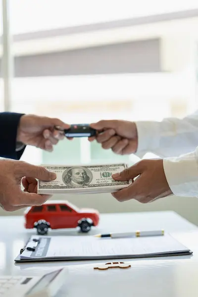 Car rental service concept Close up view of hands of representative handing car keys to customer after signing lease contract, document contract, vehicle. Sales agreement vertical picture