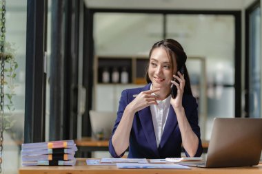 Çekici ve profesyonel Asyalı iş kadını iş ortağıyla telefonda konuşuyor ya da iş birliği ve satış anlaşmaları üzerinde pazarlık yapıyor..