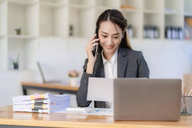Çekici ve profesyonel Asyalı iş kadını iş ortağıyla telefonda konuşuyor ya da iş birliği ve satış anlaşmaları üzerinde pazarlık yapıyor..