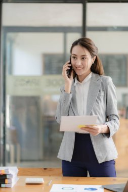 Çekici ve profesyonel Asyalı iş kadını iş ortağıyla telefonda konuşuyor ya da iş birliği ve satış anlaşmaları üzerinde pazarlık yapıyor..