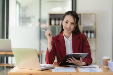 Asyalı iş kadını dizüstü bilgisayarla çalışıyor, masrafları hesaplıyor, mali rapor kağıt, grafik ve dizüstü bilgisayar yapıyor.