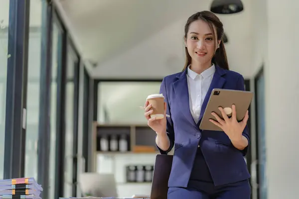 Professional business woman, corporate marketing manager, female worker holding a digital tablet is reading information of a new startup on the tablet and analyzing business strategy and planning.