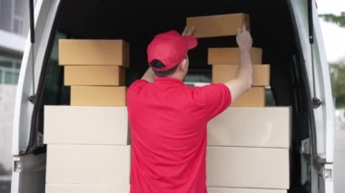 Elinde karton bir kutu tutan yakışıklı bir Asyalı arka planda minibüs olan bir evin önünde duruyor. Teslimat konsepti. 4K çözünürlüğü.