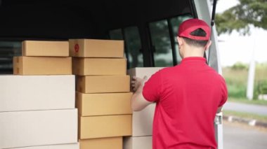 Elinde karton bir kutu tutan yakışıklı bir Asyalı arka planda minibüs olan bir evin önünde duruyor. Teslimat konsepti. 4K çözünürlüğü.