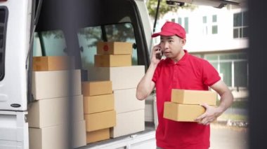 Elinde karton bir kutu tutan yakışıklı bir Asyalı arka planda minibüs olan bir evin önünde duruyor. Teslimat konsepti. 4K çözünürlüğü.