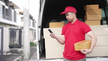 Elinde karton bir kutu tutan yakışıklı bir Asyalı arka planda minibüs olan bir evin önünde duruyor. Teslimat konsepti. 4K çözünürlüğü.