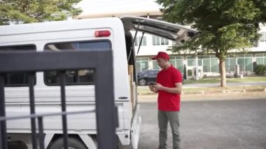 Elinde karton bir kutu tutan yakışıklı bir Asyalı arka planda minibüs olan bir evin önünde duruyor. Teslimat konsepti. 4K çözünürlüğü.