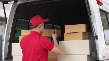 Elinde karton bir kutu tutan yakışıklı bir Asyalı arka planda minibüs olan bir evin önünde duruyor. Teslimat konsepti. 4K çözünürlüğü.