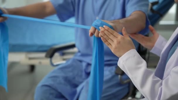 看護師は 病院で男性患者の身体療法を支援し アジアの女性理学療法士が働き 患者の手を保護するのを助けます 患者はクリニック4Kで筋肉を伸ばします — ストック動画