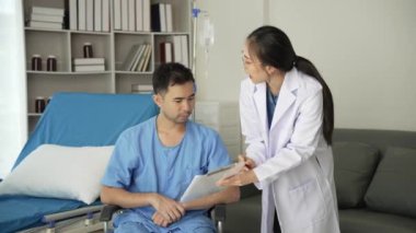 Genç Asyalı kadın doktor ve genç erkek hasta nabzını kontrol ederken yatıyorlar. Danışmak ve hemşirelerin not alıp Video 4k 'ye yardım etmelerini sağlamak.