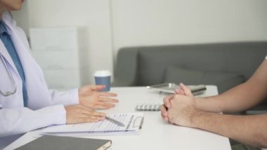 Sağlık kliniğinde muayene sırasında erkek hastayla birlikte Asyalı kadın doktor hastane ofisinde masada oturuyor.