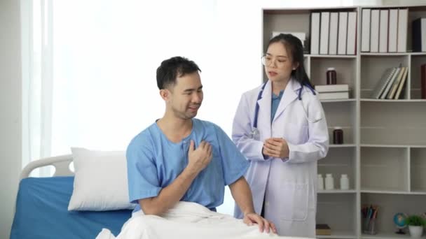 若いアジアの女性医師と若い男性患者は パルスコンサルタントをチェックしながらベッドに横たわり 看護師とノートを取ってビデオ4Kを助ける — ストック動画