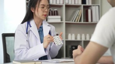 Sağlık kliniğinde muayene sırasında erkek hastayla birlikte Asyalı kadın doktor hastane ofisinde masada oturuyor.