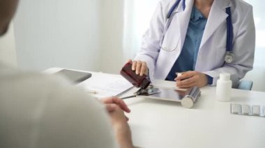 Sağlık kliniğinde muayene sırasında erkek hastayla birlikte Asyalı kadın doktor hastane ofisinde masada oturuyor.